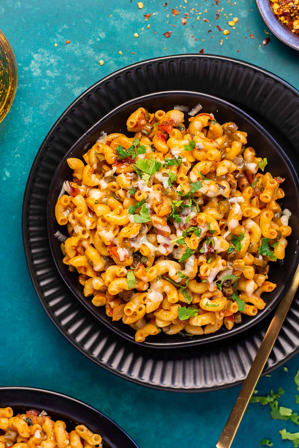 Masala macaroni topped with cheese, red pepper flakes and cilantro served in a black bowl